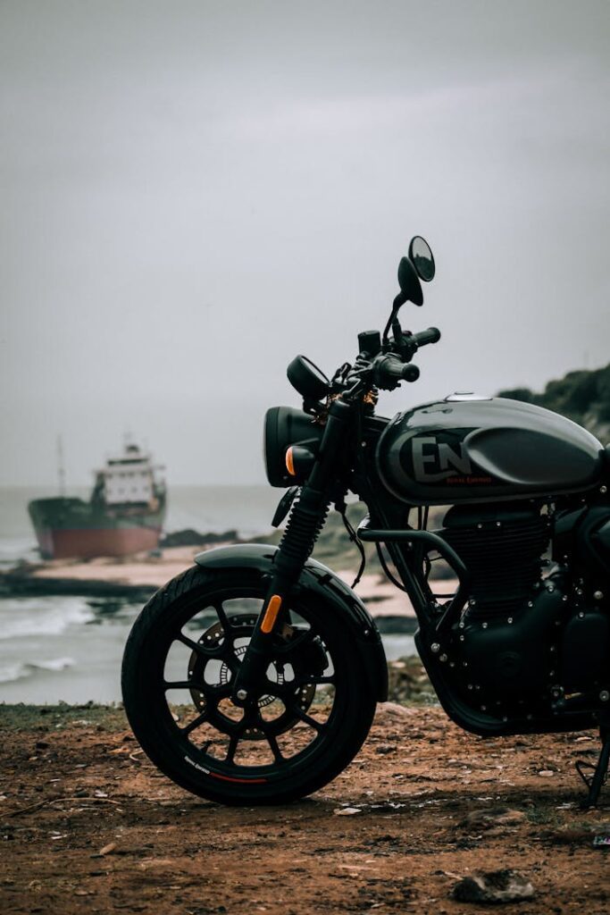 Vertical shot of a Royal Enfield motorcycle on a coast, with a ship in the background.
